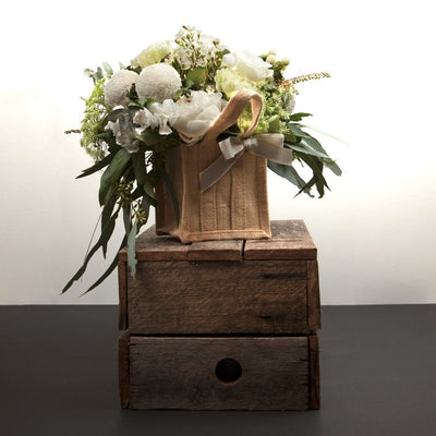 Elegant White Floral Arrangement in Hessian Bag. Mixture of pure white peonies and flowers, cream white flowers and gum leaves with luscious foliage and leaves. Available in 3 sizes small, medium, and large. Presented in our stylish environmental hessian bags.